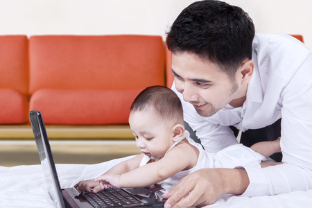 Portrait of cute baby playing laptop on the floor with his father, shot at home