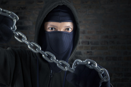 Portrait of killer holding chain in front of brick wall