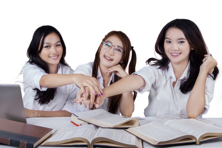 Portrait of three beautiful schoolgirls joining hands together, isolated on white backgroundの写真素材