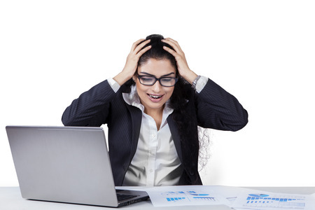 Stressful young businesswoman screaming on the table with laptop and paperwork