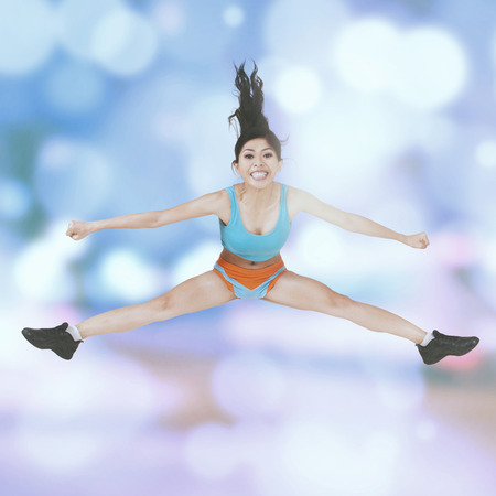 Portrait of healthy woman with sportswear, jumping with light glitter background