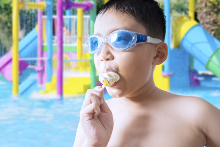 Closeup of male child wearing swimming glasses on the pool while enjoying a delicious ice creamの写真素材