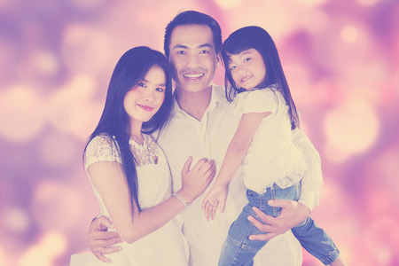 Three member of happy family smiling at the camera, shot with festive light backgroundの写真素材