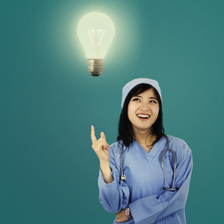 Female surgeon getting an idea and pointing at a bright light bulbの写真素材