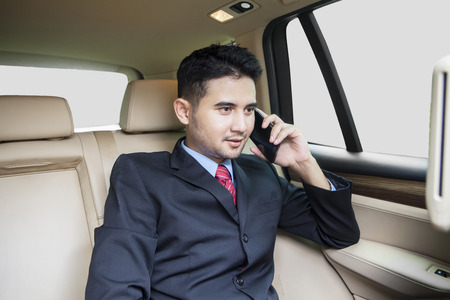 Young businessman wearing formal suit and sitting on the back seat while talking on the phone in the carの写真素材