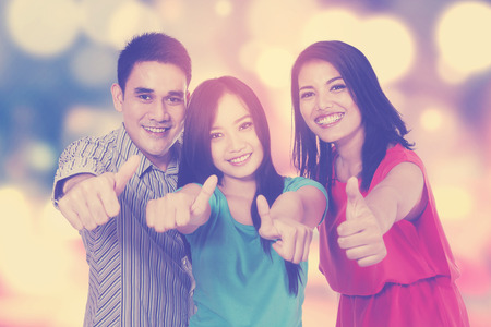 Portrait of three college students showing thumbs up on the camera, shot with bokeh backgroundの写真素材
