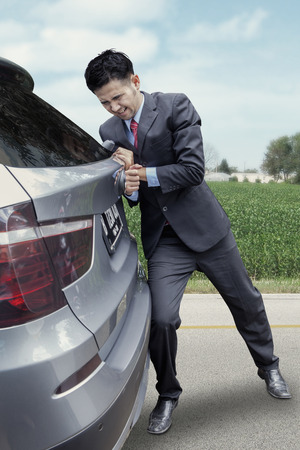 Portrait of young businessperson pushing a broken car alone on the roadの写真素材