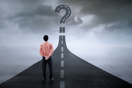Rear view of young businessman standing on the road while looking at question sign Rear view of young businessman standing on the road while looking at question sign