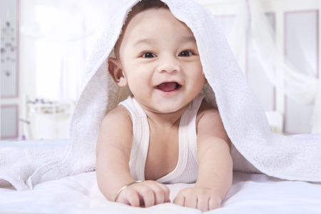 Portrait of excited innocent baby boy lying on the bedroom and laughing on the camera under a towelの写真素材