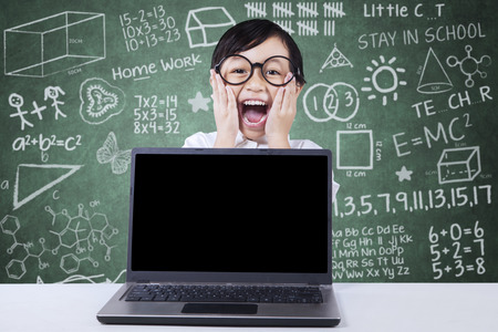 Portrait of excited female student screaming in the classroom with empty laptop screenの写真素材