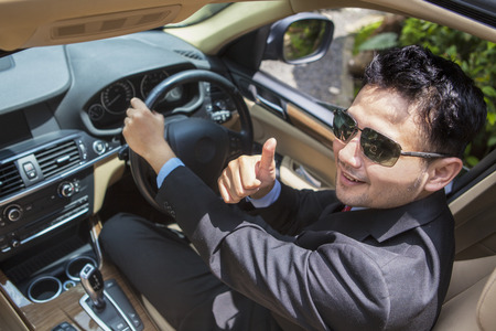 Unique perspective of successful businessman driving a new car while showing a thumb up
