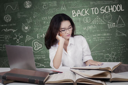 Portrait of female high school student back to school and studying in the classroom while reading...