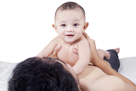 Cute baby smiling and looking at the camera while playing on the father stomach, isolated on white backgroundの写真素材