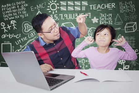 Young teacher advising his female student to study in the classroom with a book and laptopのeditorial素材