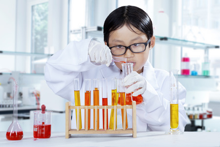 Portrait of schoolboy doing chemistry experiment while wearing coat in the laboratory
