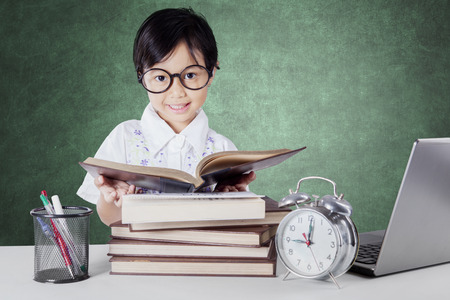 Female elementary school student back to school and reading books in the class with laptop, alarm clock, and stationery on the tableの写真素材
