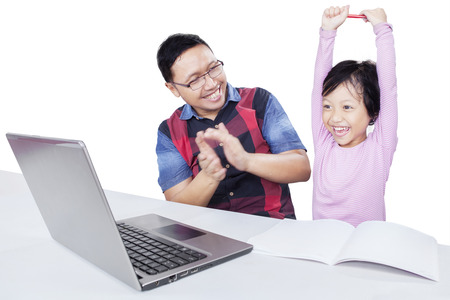 Cheerful little girl raising hands with her dad giving applause after finishing her study with...