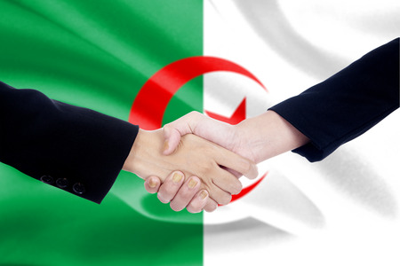 Two entrepreneurs shaking hands with algerian flag backgroundの写真素材