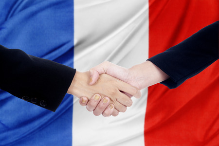 Two businesspeople closing a deal by shaking hands in front of a france flagの写真素材