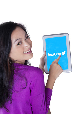 JAKARTA, SEPTEMBER 07, 2015: Sweet girl smiling at the camera while holding a digital tablet with twitter logo on the screenのeditorial素材