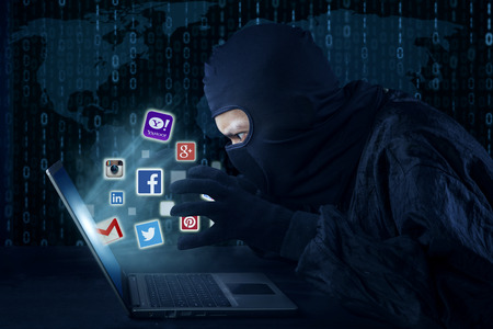 JAKARTA, SEPTEMBER 21, 2015: Male thief wearing mask and stealing information of social media account like facebook, twitter, instagram, email, and yahoo with laptopのeditorial素材