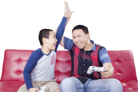 Portrait of little boy playing video game and claps hands with his dad to celebrate the winning