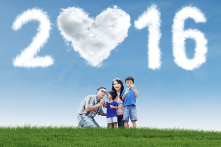 Portrait of asian family playing bubble on the meadow with cloud shaped numbers 2016 and heart symbolの写真素材