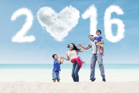 Portrait of happy family having fun on the beach with cloud shaped numbers 2016 and heart signの写真素材