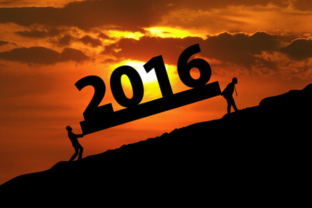 Image of two silhouette male worker carrying numbers 2016 on the hill at sunset time