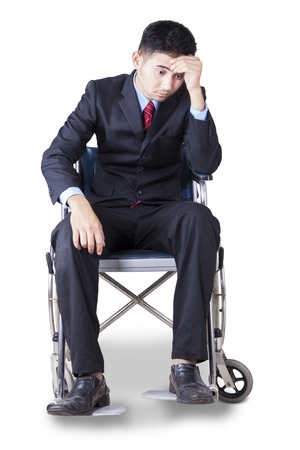 Portrait of young businessman wearing formal suit, sitting on the wheelchair and looks stressfulの写真素材