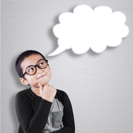 Portrait of cute little boy with casual clothes and wearing glasses, looking at empty speech bubbleの写真素材