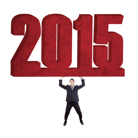 Young businessman lifts number 2015 in studio, isolated over white background