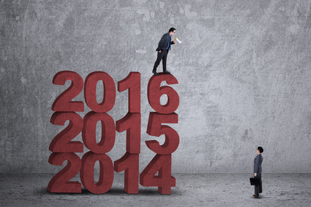 Image of young businessman standing on the numbers 2016 and using a megaphone to call his partnerの写真素材
