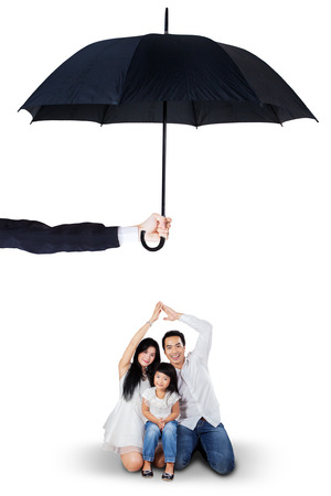 Portrait of joyful parents and their daughter sitting in the studio under umbrella. Life and family insurance conceptの写真素材