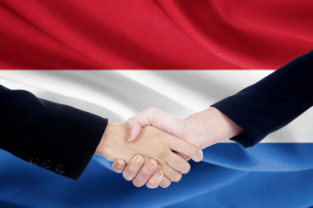 Image of two people in business suit, shaking hands in front of Netherlands national flagの写真素材