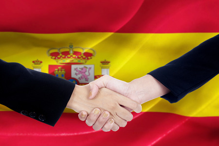 Closeup of two people with formal suit, shaking hands in front of Spanish flagの写真素材