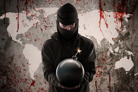 Terrorism concept: Jihadist wearing mask and holding a bomb in front of bloody world mapの写真素材