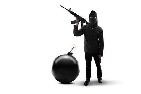 Terrorism concept: Male rebel with mask, standing in the studio with bomb and holding machine gunの写真素材
