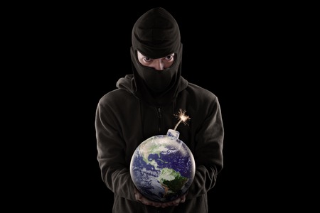 Terrorism concept: Male terrorist wearing mask and holding a bomb with globeの写真素材