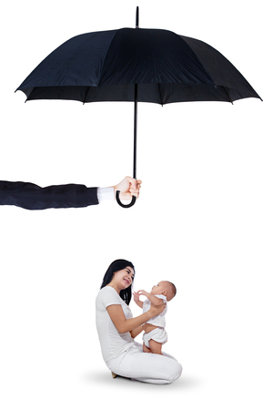 Image of young happy mother holding her little daughter in the studio under umbrella. Life and family insurance conceptの写真素材