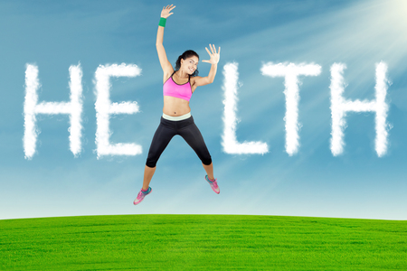 Portrait of cheerful young woman wearing sportswear, jumping on the meadow with cloud shaped health textの写真素材