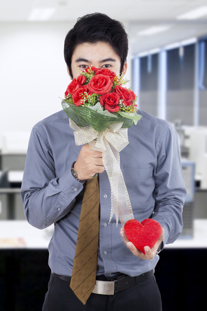 Portrait of handsome man with flowers and a gift standing at the officeの写真素材