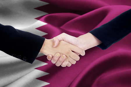Picture of agreement handshake with two entrepreneur hands, shaking hands with a Qatari flag backgroundの写真素材