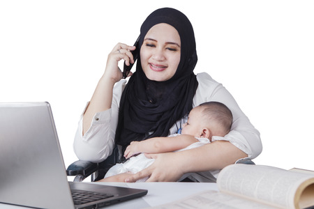 Portrait of happy muslim mother working with laptop while talking on the phone and nursing her babyの写真素材