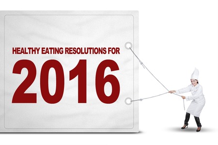 Picture of female chef wearing uniform and pulls a big board with a text of healthy eating resolutions for 2016の写真素材