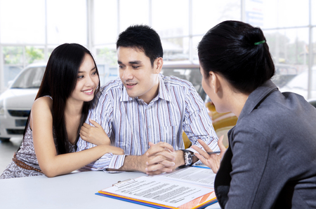 Picture of two young car buyers discussing with a female car dealer in the showroomの写真素材