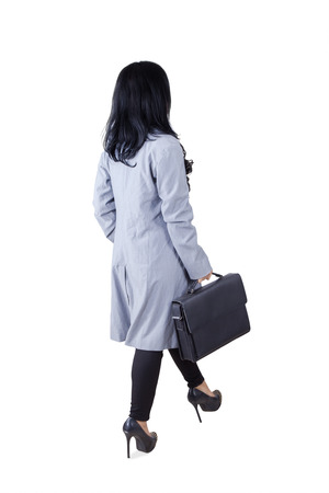 Back view of female worker with long hair, walking in the studio while carrying a briefcaseの写真素材