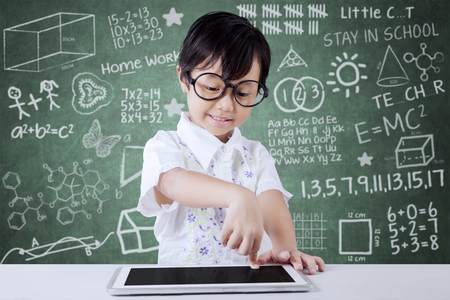 Little girl touching a digital tablet screen on the tablet in the classroom at schoolの写真素材