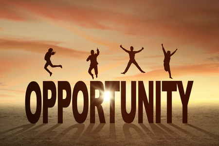 Silhouette of four entrepreneurs jumping over a text of opportunity at sunset timeの写真素材