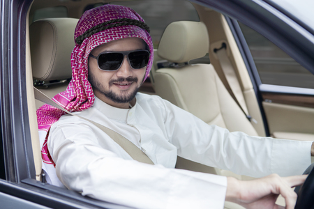 Successful Arabic businessman driving a car while wearing sunglasses and headscarfの写真素材